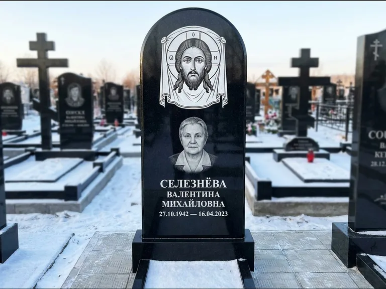 Памятник с гравировкой иконы: небольшая скромная одиночная стела с именной иконой — золочёный нимб на образе, аккуратный участок с газоном, работа «Ковалёв» в Саратове