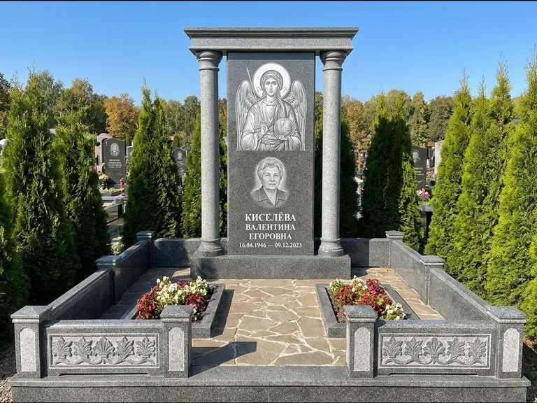 Памятник с гравировкой иконы: массивная стела с двускатным навершием-домиком — гравировка Николая Чудотворца, живая изгородь из туи, работа «Журавлёв» в Саратове