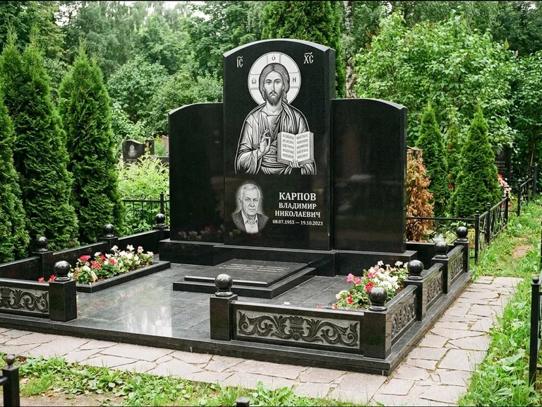 Памятник с гравировкой иконы: широкая панорамная стела с золочёным нимбом — гравировка образа Матроны Московской, цветник с белыми хризантемами, работа «Мельникова» в Саратове